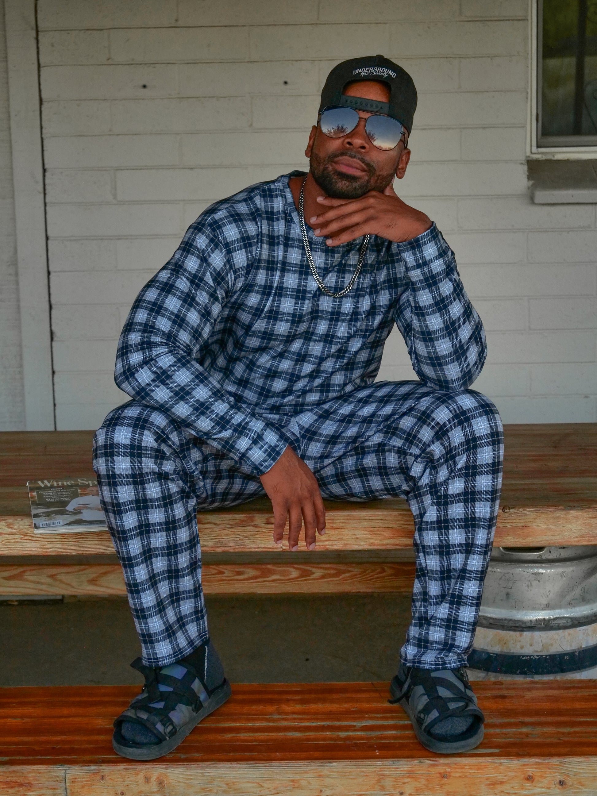 Man seating and dressed in a black and white plaid sweatshirt and jogger outfit