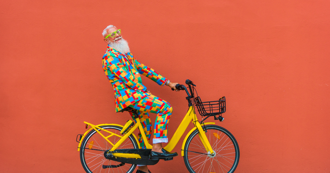 Man with long white beard and a colorful jacket riding a yellow bike