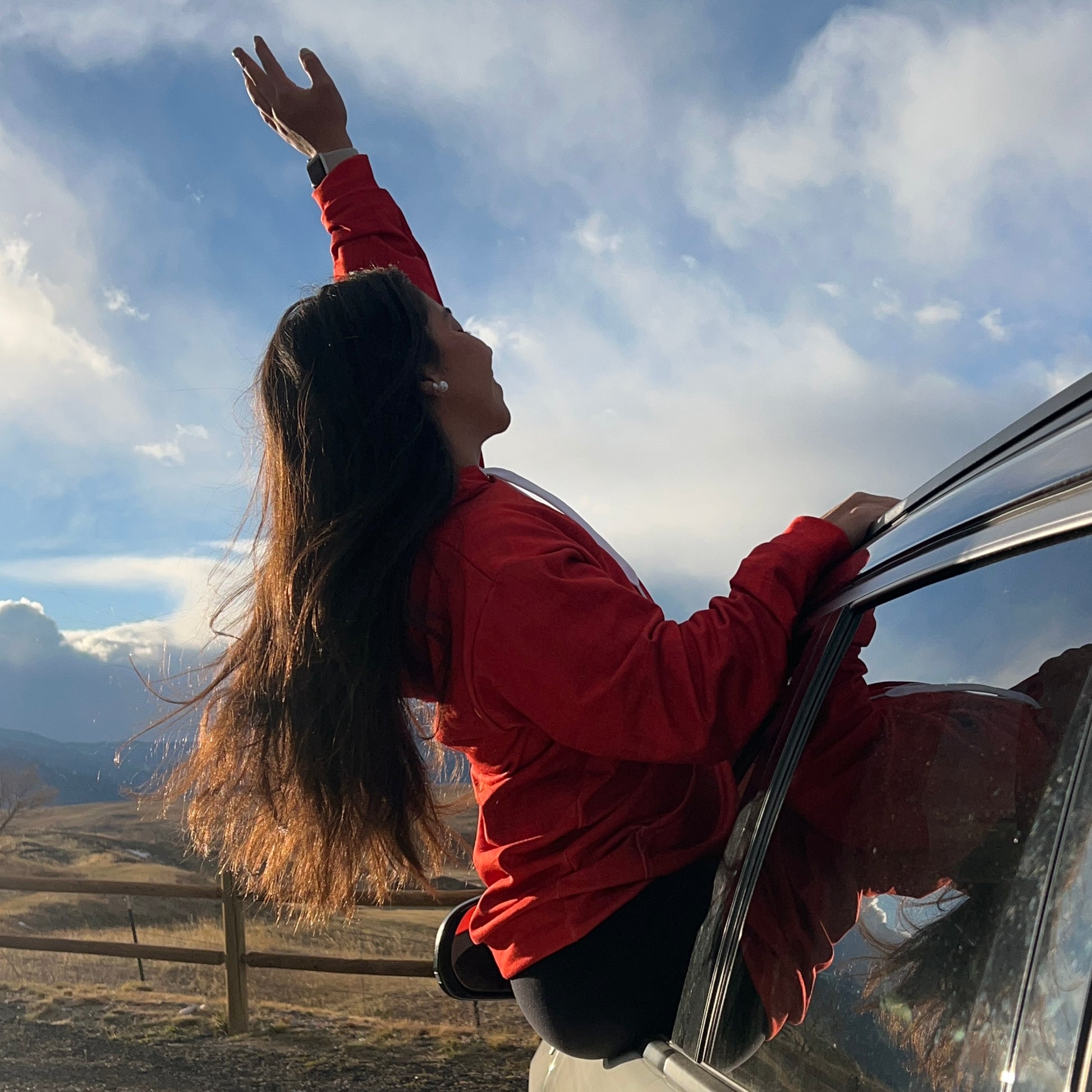 Woman seating through a car window and wearing a lava red hoodie